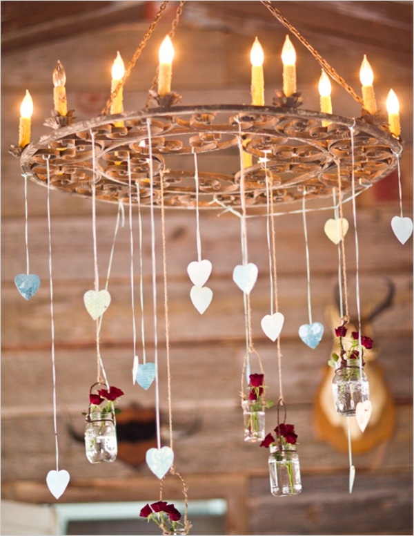 a wedding chandelier with candle like bulbs, hearts hanging down and bottles with deep red blooms
