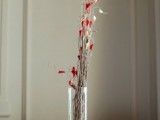 a simple wedding centerpiece of a clear vase, branches and red blooms
