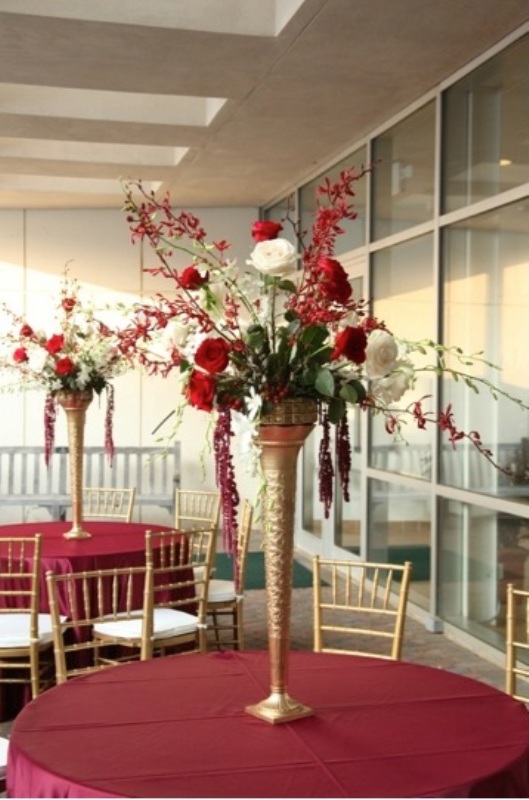 a tall wedding centerpiece of a gold tall vase and greenery, white and deep red blooms