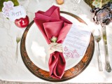 a metal charger, a white plate and a burgundy napkin accented with rope and a flower