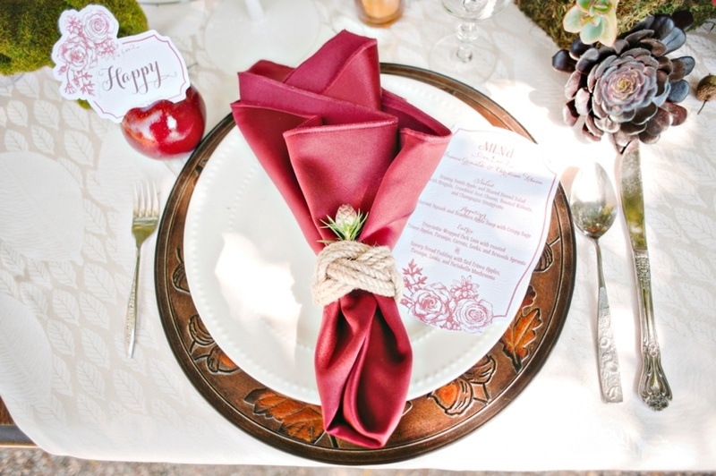 a metal charger, a white plate and a burgundy napkin accented with rope and a flower