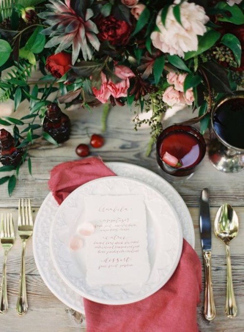a deep red glass, a muted red napkin and a floral centerpiece with burgundy blooms accent the fall tablescape