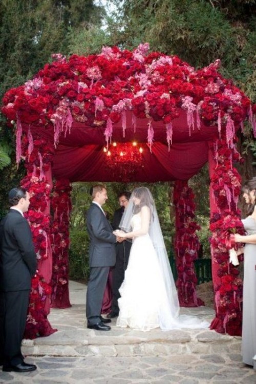 a deep red arch decorated with blooms and fabric will make your couple stand out a lot