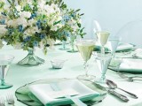 a green and white wedding tablescape with white and blue blooms and greenery, green glass plates, mint napkins with ribbons