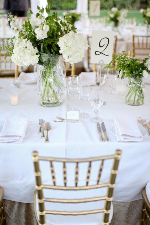 a fresh spring wedding tablescape with white linens, white blooms and greenerycandles and white napkins is amazing
