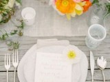 a neutral spring wedding tablescape with a white table runner, super bold blooms and greenery and white plates and napkins