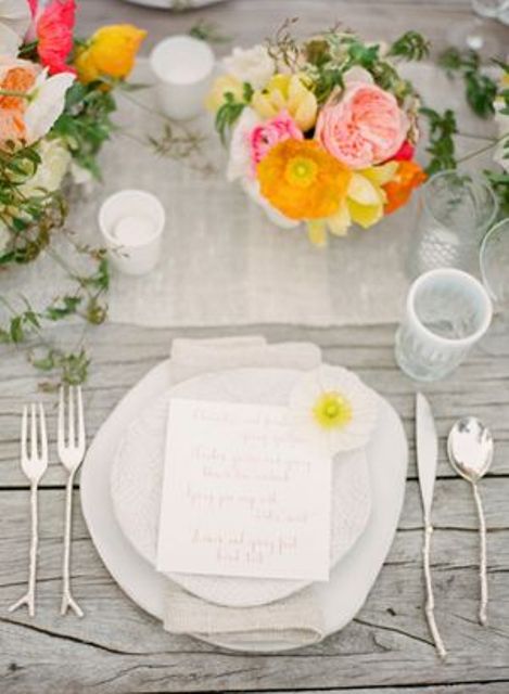 a neutral spring wedding tablescape with a white table runner, super bold blooms and greenery and white plates and napkins