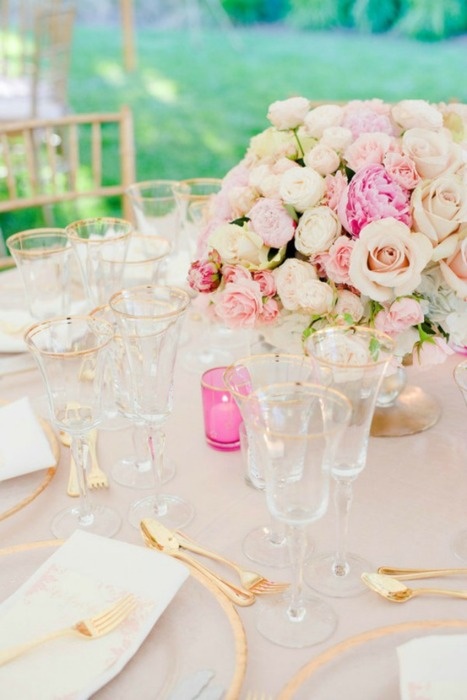 an elegant neutral wedding tablescape with a blush tablecloth, clear chargers with a gold rim, gold hem glasses, a neutral rose centerpiece with hot pink ones and a hot pink candleholder