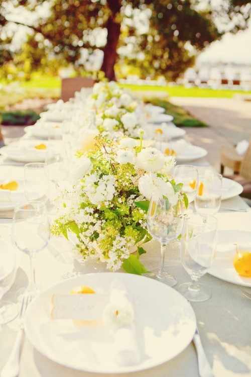 a neutral and fresh spring wedding tablescape with yellow and white blooms and greenery, white plates and napkins and pears