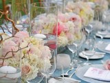 a pastel wedding tablescape with a blue tablecloth, white and blush blooms, branches, frosted candleholders