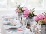 a spring wedding tablescape with peonies and greenery, white and blue plates and white napkins, neutral and pink frosted cupcakes is very sweet