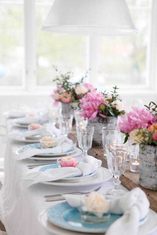 a spring wedding tablescape with peonies and greenery, white and blue plates and white napkins, neutral and pink frosted cupcakes is very sweet