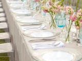 a neutral spring wedding tablescape with clear plates, pink and white blooms in jars and blue glasses