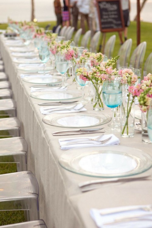 a neutral spring wedding tablescape with clear plates, pink and white blooms in jars and blue glasses