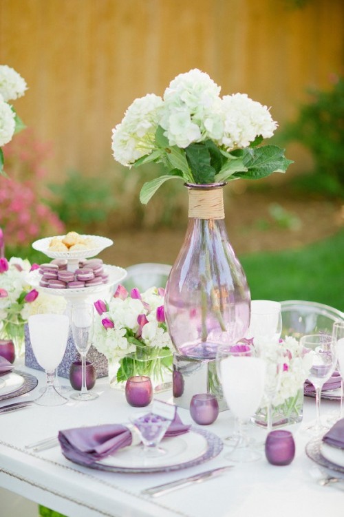 a lovely purple and white wedding tablescape with white and fuchsia blooms and greenery, purple glasses and napkins, lilac chargers is amazing