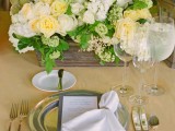 an elegant and chic spring wedding tablescape with a lush white and yellow rose and greenery wedding centerpiece, shiny plates and vintage silver cutlery