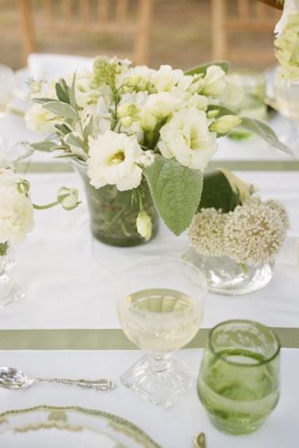 a green and white wedding tablescape with white blooms and greenery, green rim plates and green glasses is calm and cool