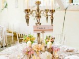 a pastel wedding tablescape with pink blooms and greenery, a tall candelabra, a blush tablecloth and neutral napkins