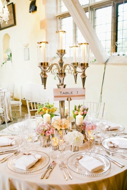 a pastel wedding tablescape with pink blooms and greenery, a tall candelabra, a blush tablecloth and neutral napkins