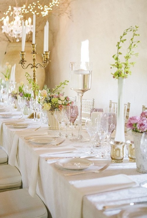 a sophisticated neutral wedding tablescape with pink and neutral blooms and greenery, tall and thin candles and white porcelain and linens