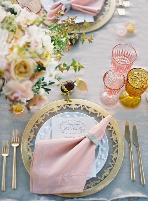 a pastel spring wedding table setting with a grey tablecloth, blush blooms, pink and amber glasses and a pink napkin