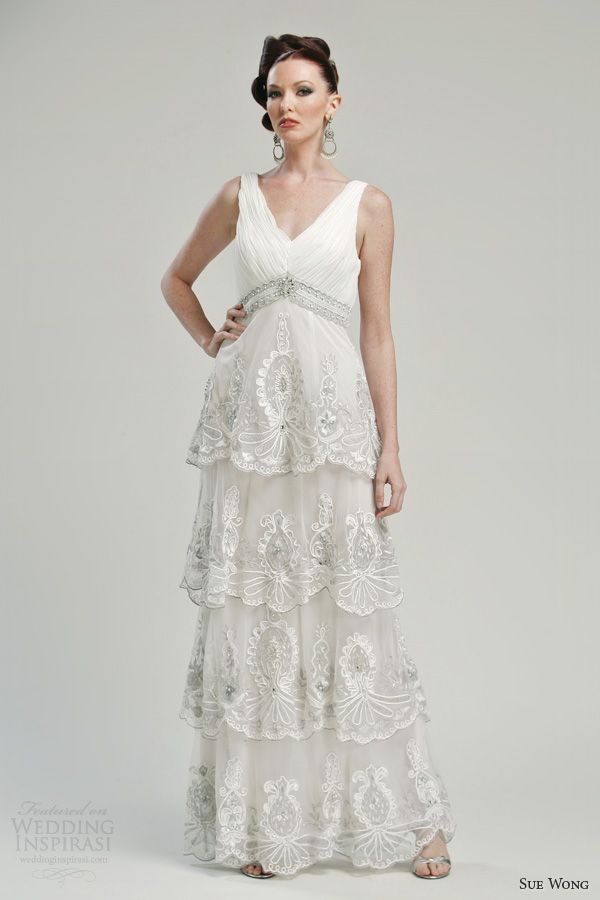 An A line wedding dress with ruffles, embellishments, a deep V neckline and no sleeves, an embellished waist for a vintage look