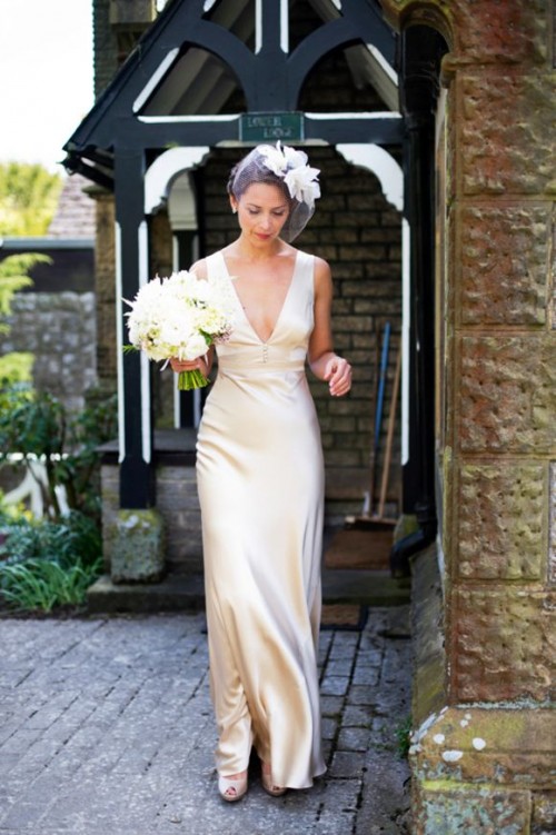 a vintage-inspired silk wedding dress with a deep neckline, no sleeves, a birdcage veil with a faux bloom and chic neutral shoes for a vintage-inspired bridal look