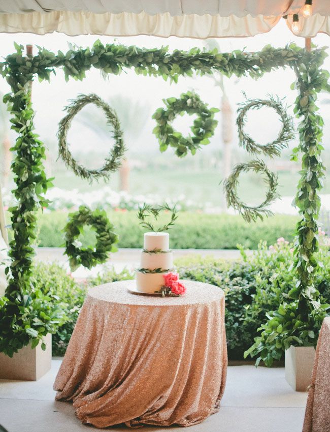 a greenery wedding arch with an assortment of greenery wreath doubles as a wedding dessert table backdrop