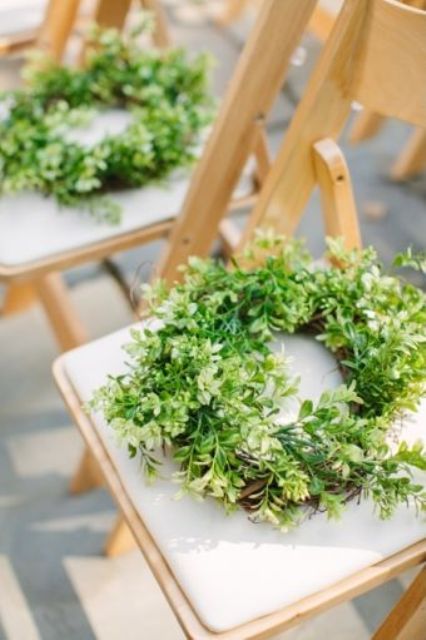 a lush greenery wreath to mark a chair is a cool idea to refresh your wedding ceremony space or venue