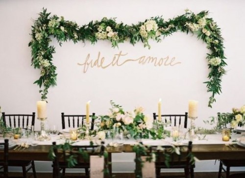a lush greenery and white blooms garland on the wall match the centerpieces and make the venue look fresh and beautiful