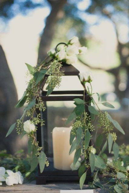 decorate a candle lantern with greenery and white blooms to make it feel outdoorsy and spring like