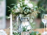 an elegant greenery and white bloom wedding centerpiece plus greenery on the table is a chic idea for a spring table