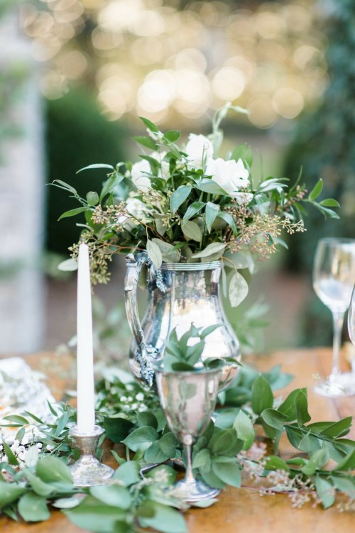 an elegant greenery and white bloom wedding centerpiece plus greenery on the table is a chic idea for a spring table