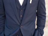 a navy three-piece suit, a white shirt, a printed bow tie and a white boutonniere