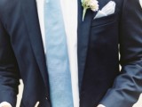 a navy suit, a white shirt, a light blue tie and a neutral boutonniere for a simple, elegant groom’s look