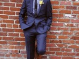 a navy suit, a navy and white plaid shirt, a black tie, brown shoes and a bright floral boutonniere