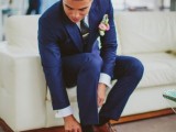 a navy suit, a white shirt, a black tie and brown shoes plus a pink boutonniere