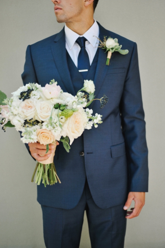 A navy three piece suit, a white shirt and a navy tie plus a boutonniere for a bold and stylish look