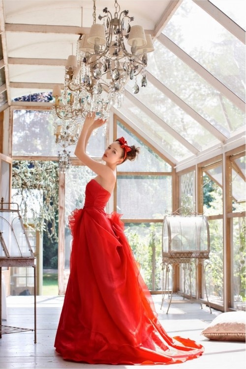 a strapless hot red wedding dress with a draped bodice, a layered skirt with a flower on the back and a train plus a red bow headpiece