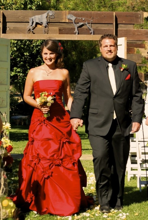 a burgundy strapless wedding dress with a draped bodice and a layered skirt, red blooms in the hair is a fantastic idea