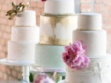white cake stands and an assortment of various pastel and metallic wedding cakes with pink blooms