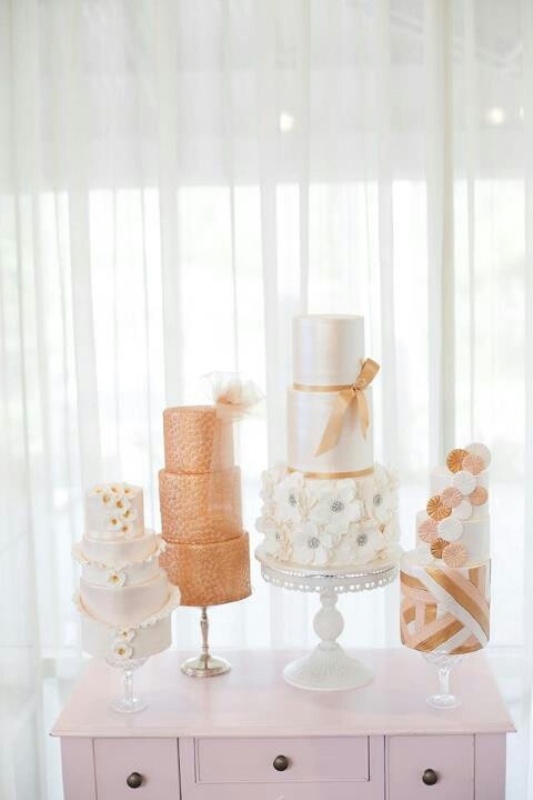 white and sheer glass cake stands with an assortment of peachy and white wedding cakes with ribbons