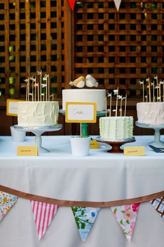 Blue, turquoise and wooden cake stands and an assortment of pastel wedding cakes with cute toppers