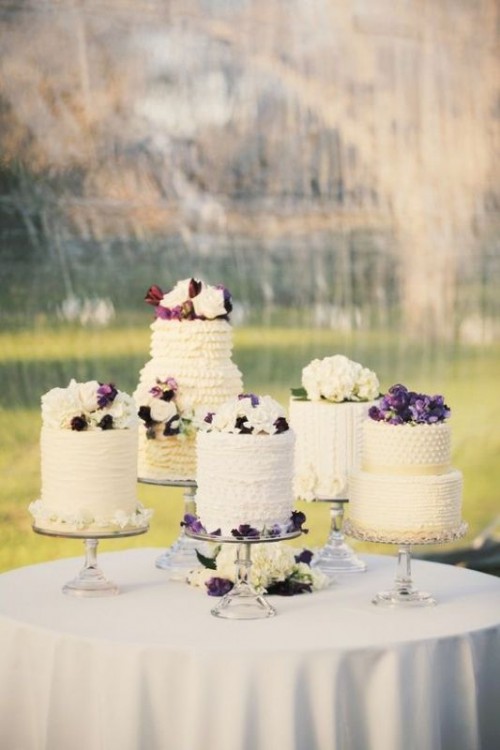 sheer glass cake stands with an assortment of ruffled wedding cakes topped with white and purple blooms
