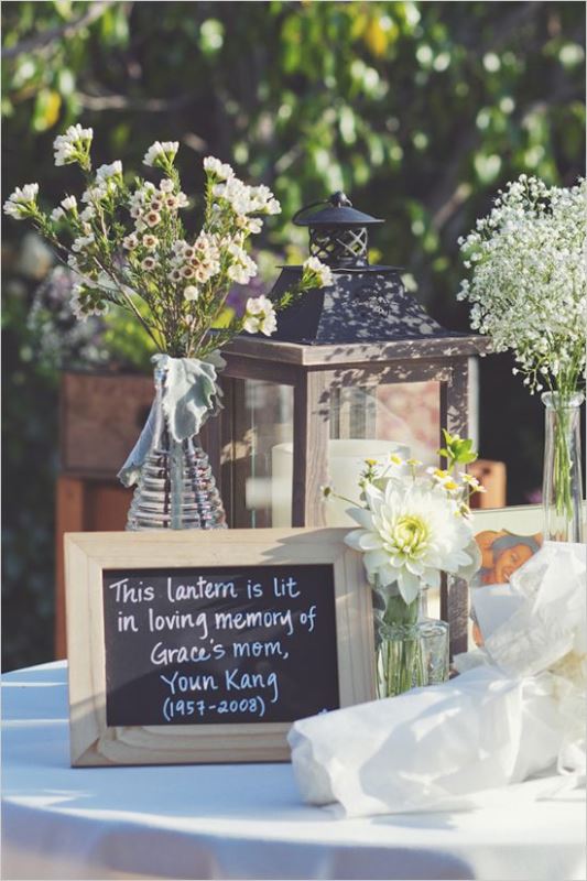 a rustic wedding table with blooms, candles and a sign that is telling about lighting the lantern in memory of a person who is gone