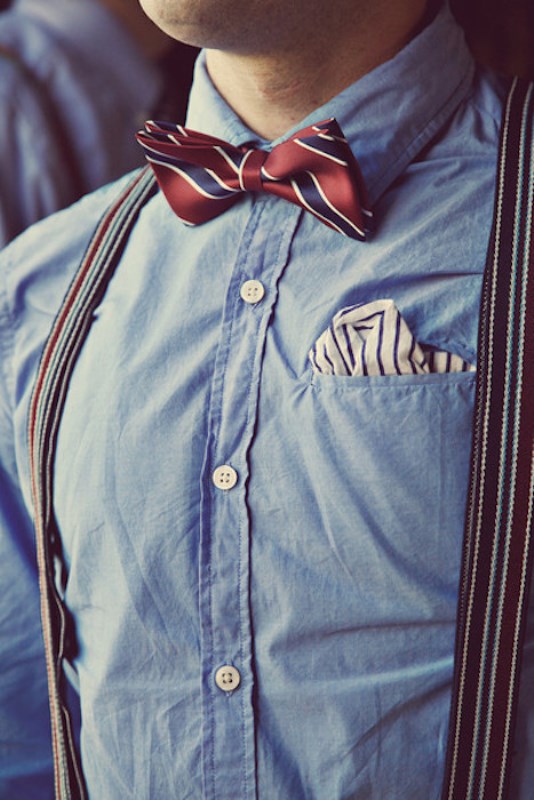 A catchy groom's look with a blue shirt, a pocket square with a striped handkerchief and a bright bow tie and bright suspenders