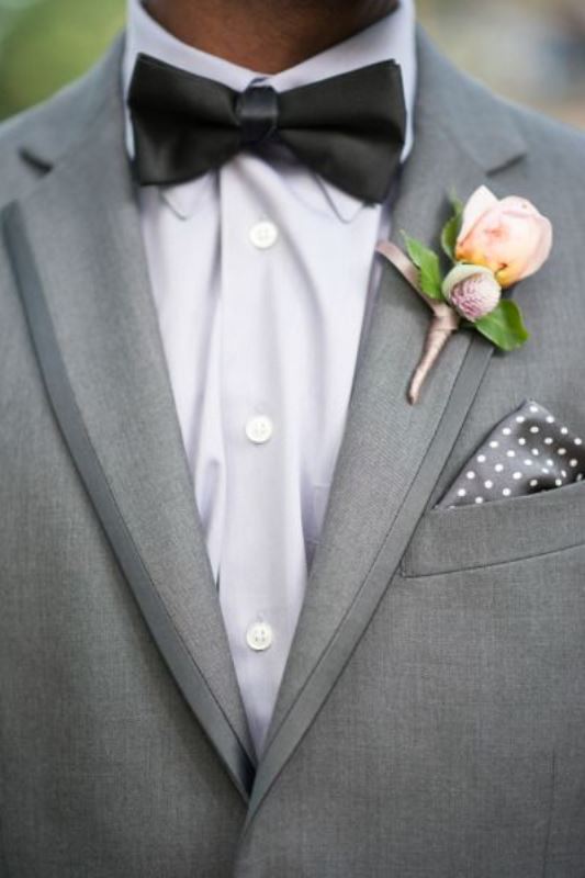 A refined modern groom's look with a grey suit, a white shirt, a black bow tie, a grey polka dot handkerchief and a delicate floral boutonniere