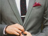 a bold and playful groom’s outfit with a grey suit, a white shirt, a black polka dot tie, a bold red printed handkerchief and a red badge as a boutonniere