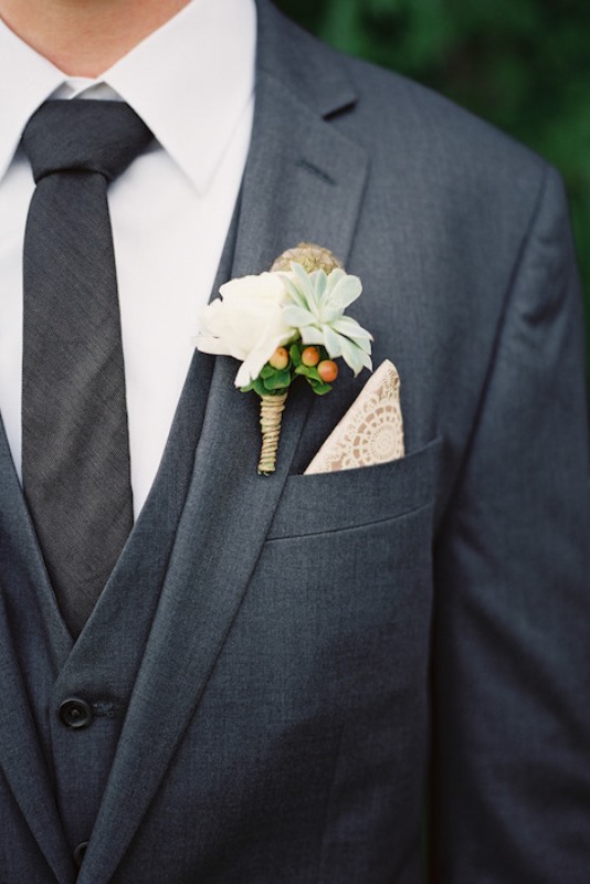 A laconic groom's look with a graphite grey three piece suit, a white shirt, a thin tie, a white floral boutonniere and a doily pocket square is chic