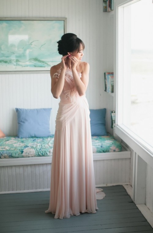 a whimsy blush wedding dress with a draped bodice and feathers on it and a pleated skirt